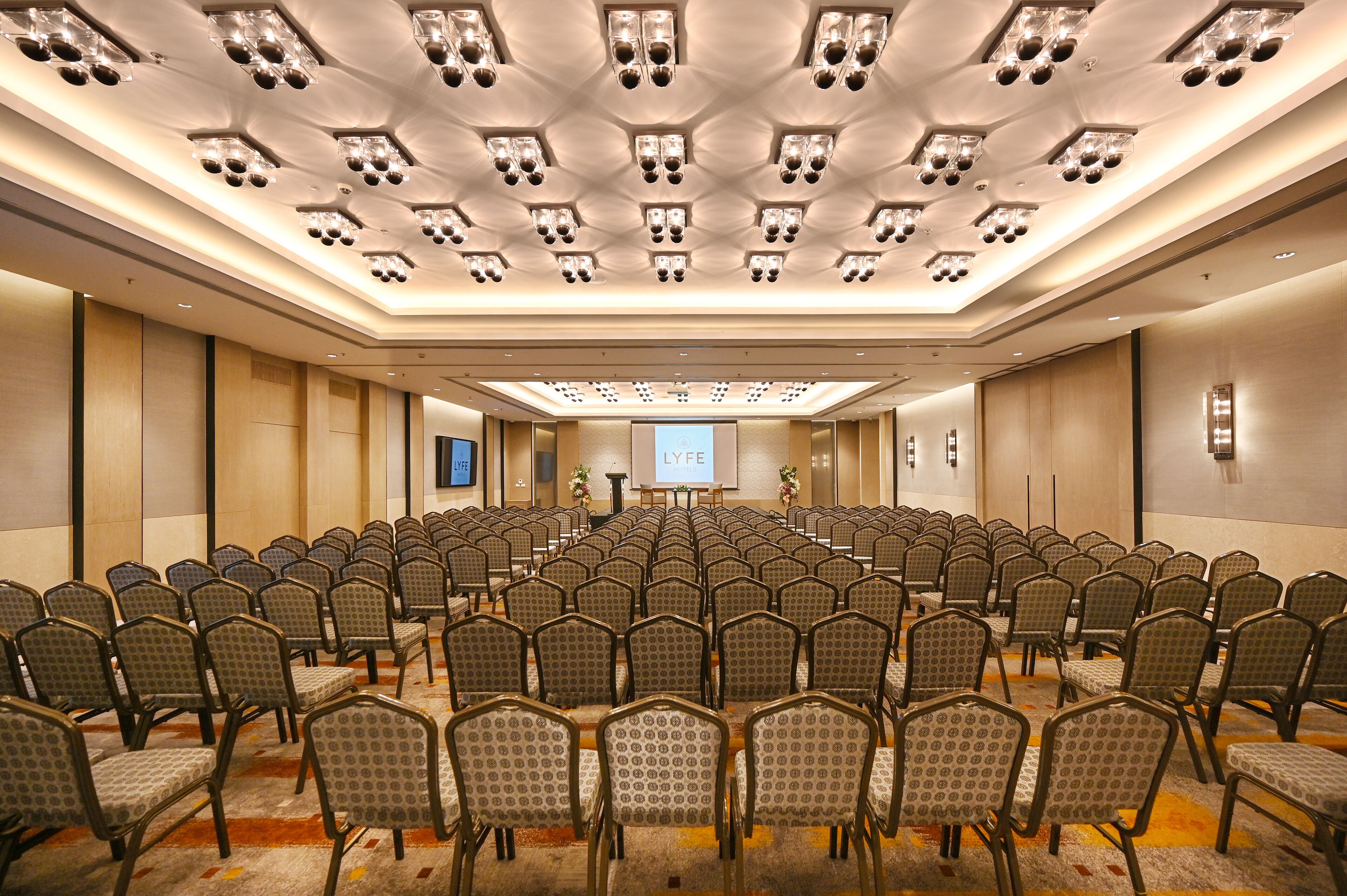 A conference room with rows of chairs, a stage with a podium, and a large screen.