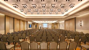 A conference room with rows of chairs, a stage with a podium, and a large screen.