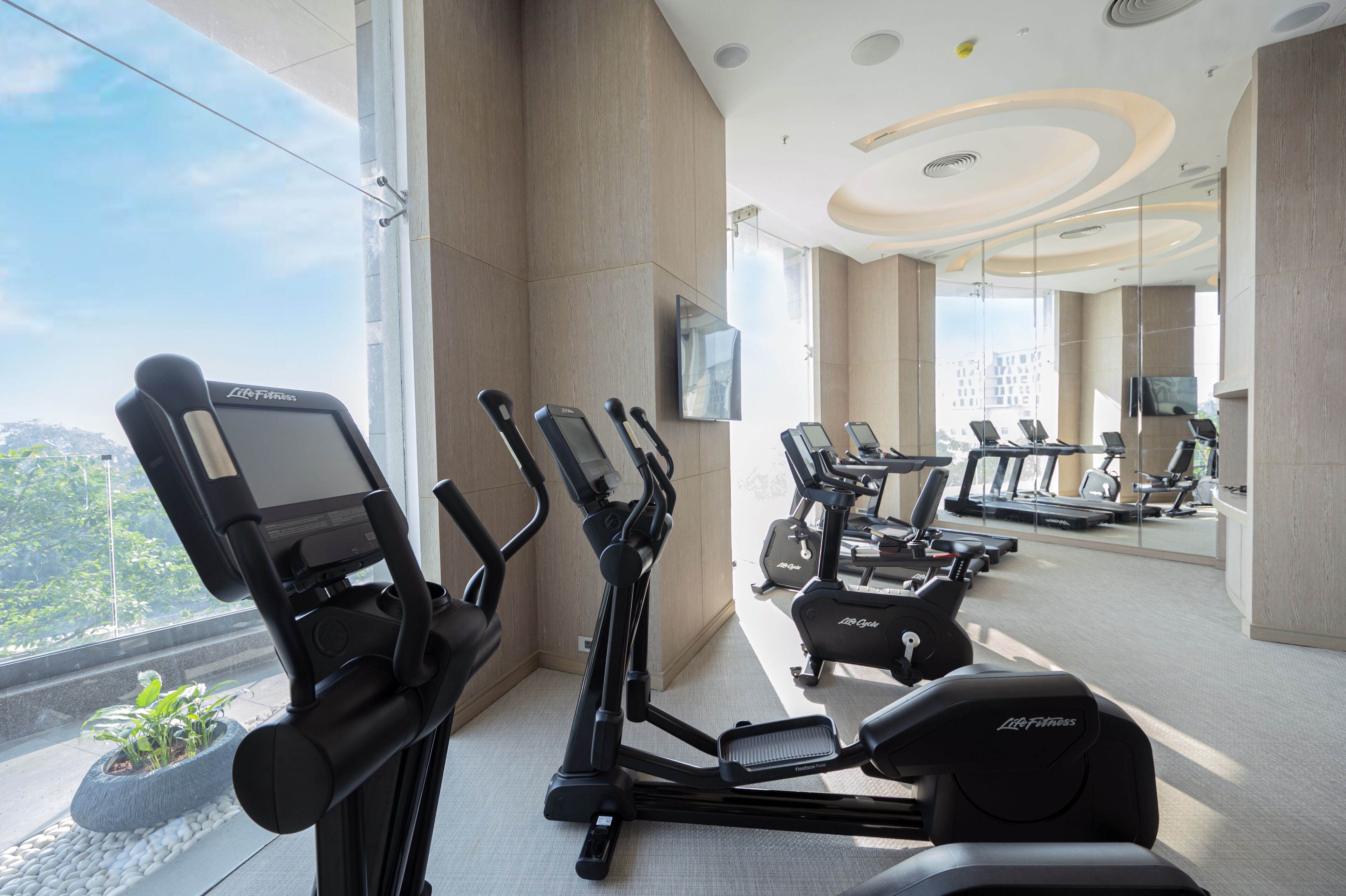 A modern gym with various exercise equipment, large windows, and a view of the outdoors.
