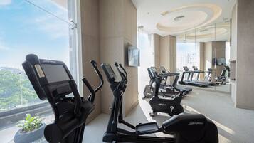 A modern gym with various exercise equipment, large windows, and a view of the outdoors.