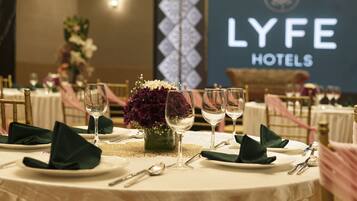 A table set for a formal dining experience with a floral centerpiece, silverware, and glassware, in a room with a 'LYFE HOTELS' sign in the background.