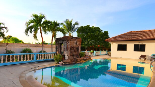 A swimming pool with a stone structure, palm trees, and a building with a tiled roof.