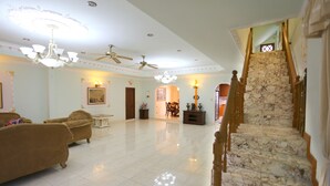 A spacious living area with a marble staircase, multiple sofas, and ceiling fans.