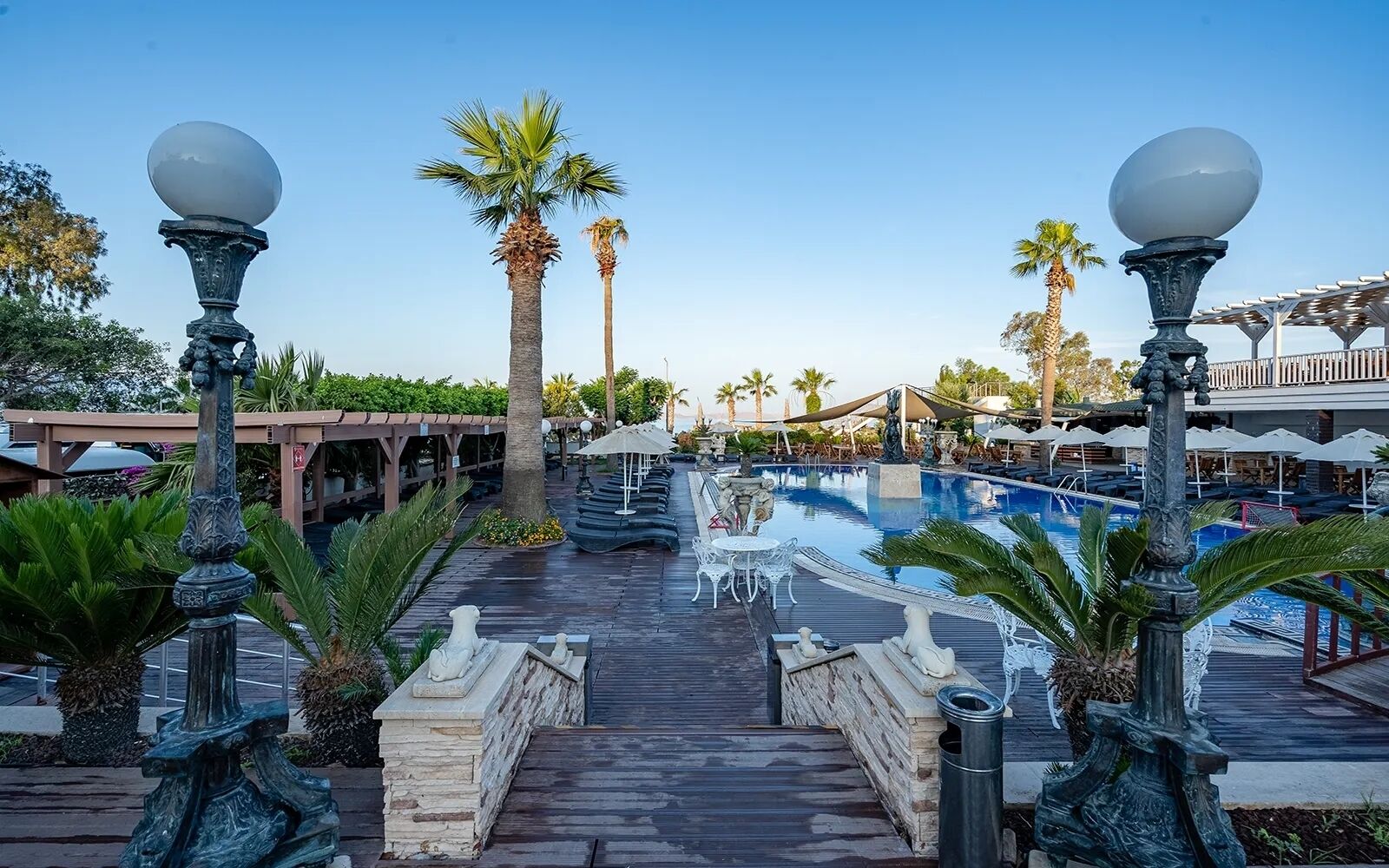 A resort pool area with a wooden deck, palm trees, and outdoor seating.