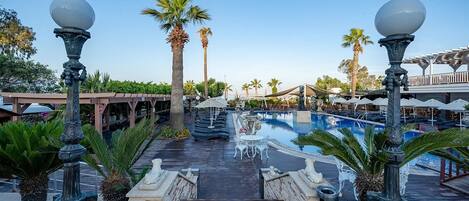 A resort pool area with a wooden deck, palm trees, and outdoor seating.