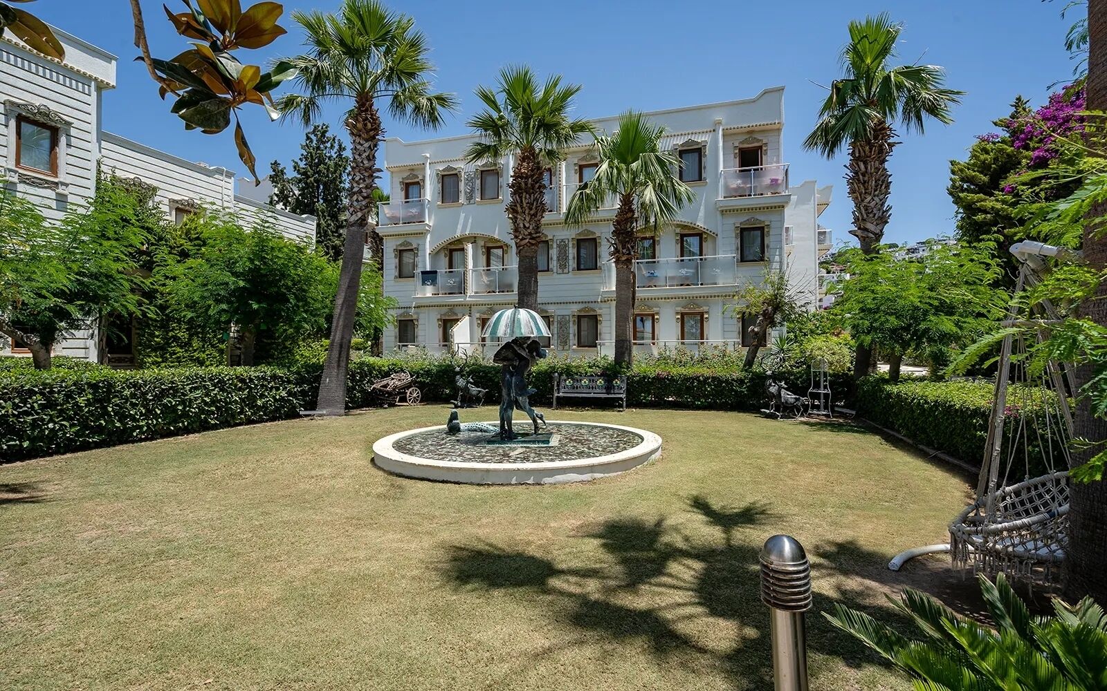 A courtyard with a statue, palm trees, and a building with balconies.
