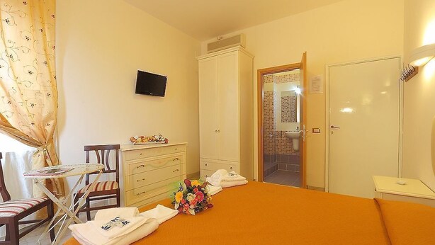 Ein Hotelzimmer mit einem Bett, einem Schreibtisch mit Stuhl, einem Kleiderschrank und einem durch eine offene Tür einsehbaren Badezimmer.