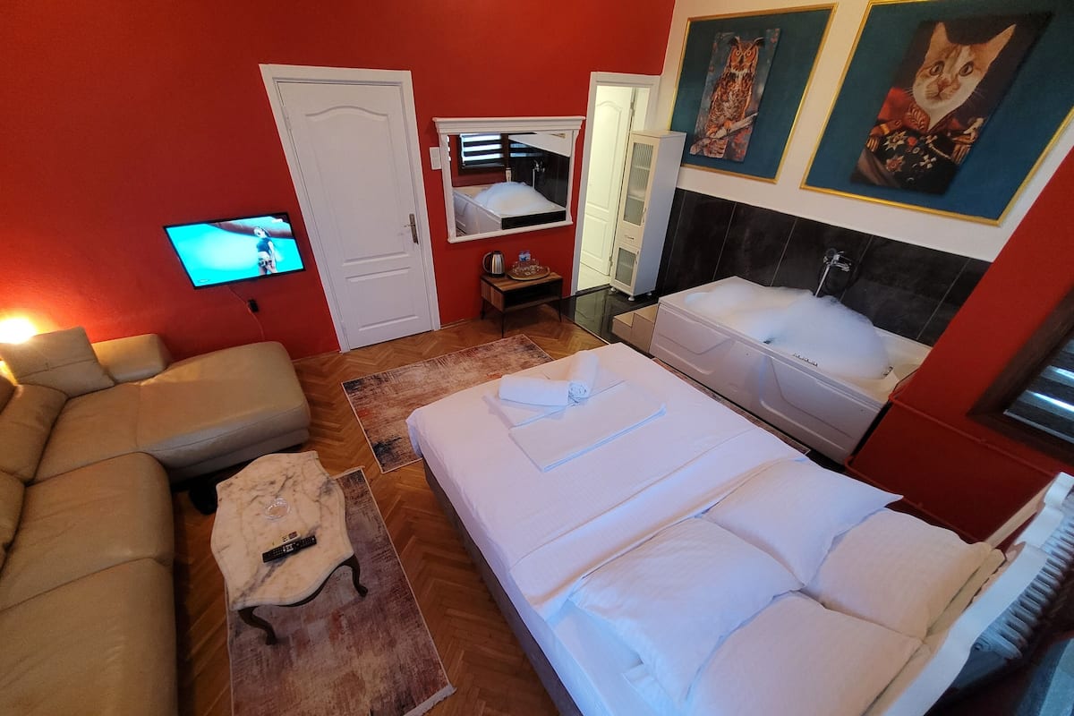 A hotel room with a bed, a sofa, a TV, a bathroom, and a mirror.
