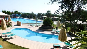 Une piscine entourée de verdure, avec des chaises longues et des parasols, sous un ciel dégagé.