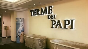 Un mur sur lequel on peut lire l’inscription « TERME DEI PAPI » et deux grandes baignoires d’aspect rustique.