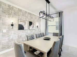 Un comedor con una mesa rectangular, seis sillas, una lámpara moderna y arte abstracto en la pared.