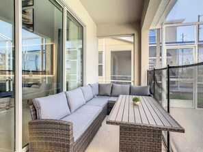 A balcony with a wicker sofa, a wooden table, and a view of the outside.