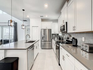 A modern kitchen with stainless steel appliances, white cabinetry, and a large island with a sink.