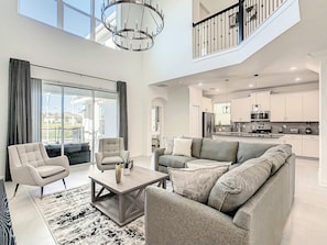 A spacious living area with a sofa, armchairs, and a coffee table, a kitchen with modern appliances, and a balcony with curtains.