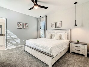 Une chambre à coucher avec un lit, des tables de chevet, un ventilateur de plafond et des œuvres d’art accrochées aux murs.
