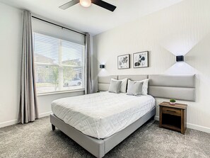 A bedroom with a bed, a nightstand, a ceiling fan, a window with curtains, and two wall-mounted lamps.