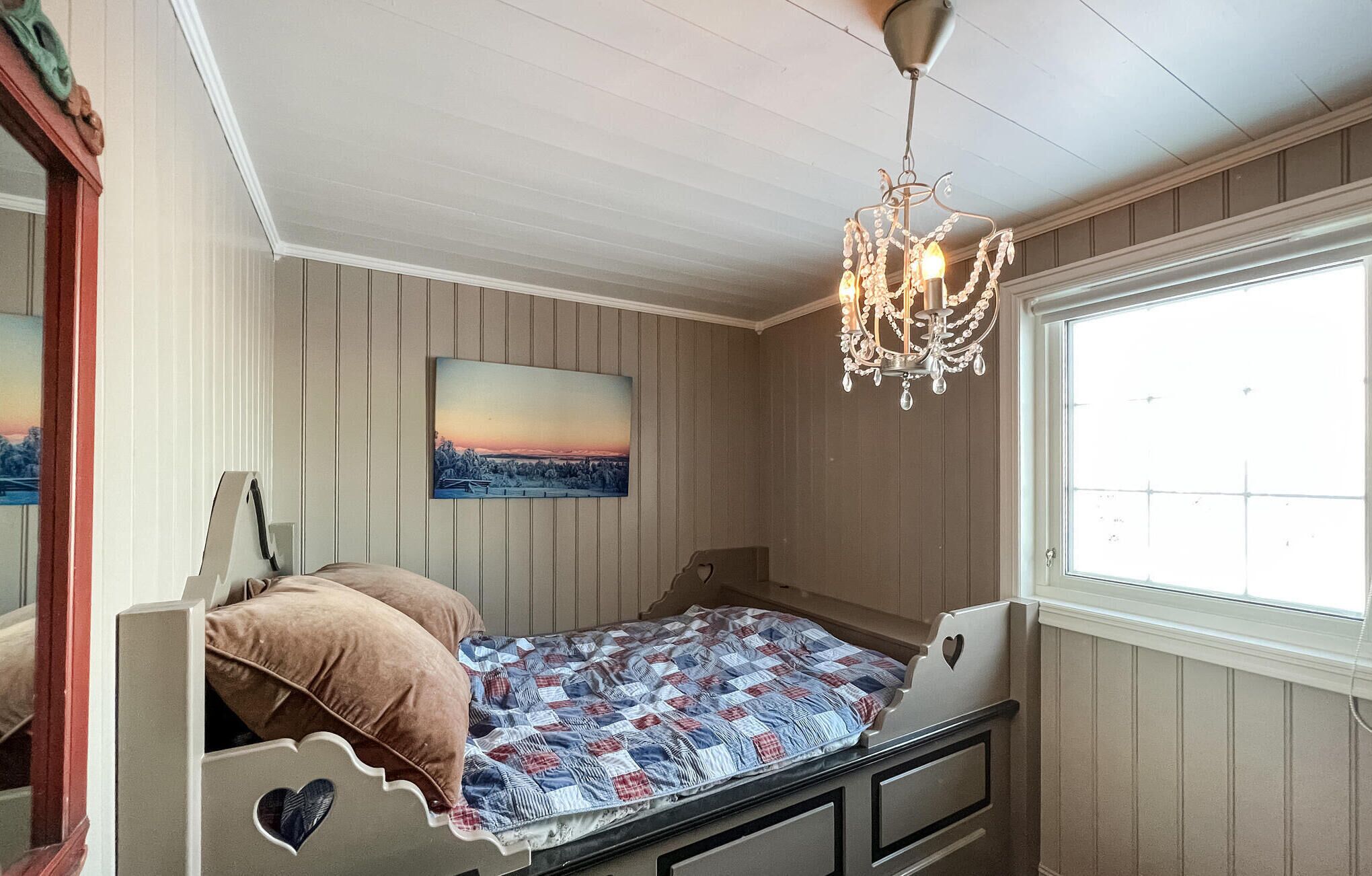 Un dormitorio con cama, candelabro, ventana y un cuadro en la pared.