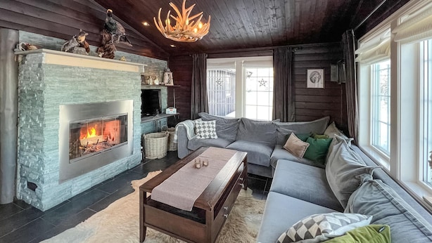 A cozy living room with a stone fireplace, a grey sofa, a wooden coffee table, and a chandelier.