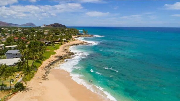 Zona costera con playa, aguas azules cristalinas y una combinación de paisajes residenciales y naturales.