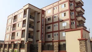 A multi-story residential building with a beige facade, red accents, and balconies. - Kans Krib (Accra)