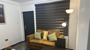 A modern living room with a sofa, decorative pillows, a glass coffee table, a lamp, and a door. - Kans Krib (Accra)