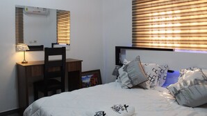 A bedroom with a bed, a desk, a chair, and a window with blinds. - Kans Krib (Accra)