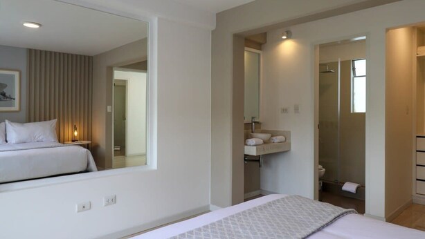 A modern hotel room with a large bed, a bedside table, a mirror, a built-in shelf with toiletries, and a shower area. - w* | Engaging 3BR with Balcony in Barranco (Barranco)