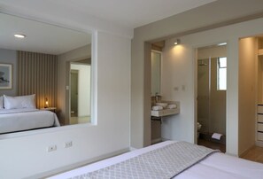 Ett modernt hotellrum med en stor säng, ett sängbord, en spegel, en inbyggd hylla med toalettartiklar och en duschhörna.