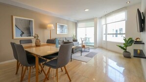 A modern living room with a dining area, large windows, and minimalist decor. - w* | Engaging 3BR with Balcony in Barranco (Barranco)