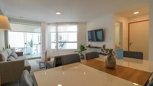 A modern living room with a large white table, grey sofas, and a TV mounted on the wall. - w* | Engaging 3BR with Balcony in Barranco (Barranco)