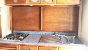 A kitchen with wooden cabinets, a gas stove, and a stainless steel sink. - 5 Suite Grecale, primo piano, balcone di 25 mq lato interno, molto silenzioso (Cecina)