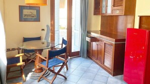 A compact kitchen with a dining table, chairs, a red refrigerator, wooden cabinets, and a hanging lamp. - 5 Suite Grecale, primo piano, balcone di 25 mq lato interno, molto silenzioso (Cecina)