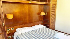 A hotel room with a wooden headboard, two bedside lamps, a checkered bedspread, and neatly folded towels. - 5 Suite Grecale, primo piano, balcone di 25 mq lato interno, molto silenzioso (Cecina)