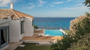 Een modern huis met een zwembad, uitzicht op zee en een balkon met lounge stoelen.