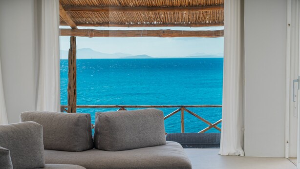 Een kamer met uitzicht op zee, een houten terras en een bank.