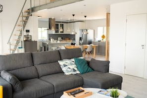 A modern living room with a grey sofa, a coffee table, and a staircase leading to a kitchen area. - Villa Yasmina - Amazing view of the sea (Estoi)
