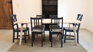 Ein Essbereich mit einem rechteckigen Tisch, der von sechs Stühlen umgeben ist, einem schwarzen Bücherregal und einer Holztür mit geometrischem Dekor.