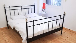 Ein Zimmer mit einem Einzelbett, dessen Gestell aus schwarzem Metall, die Bettwäsche weiß und der Boden aus Holz ist.