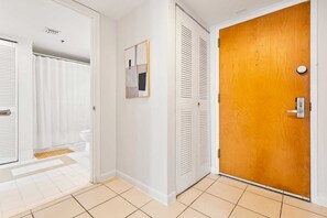 Un couloir avec une porte en bois, des murs blancs et un sol carrelé.