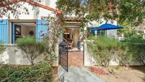 Une maison avec un patio, un coin repas et un parasol bleu.