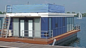 A floating house with a deck, a covered upper deck, and a view of the water. - Floating 44 Komfortable Hausboote bei Xanten mit Tollem Seeblick (Xanten)
