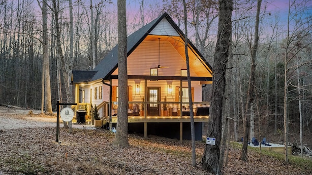 Une cabane avec une façade en bois, une véranda illuminée et une vue sur la forêt environnante.