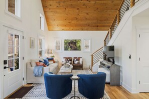 A spacious living room with a high wooden ceiling, a sofa set, a coffee table, and a television.