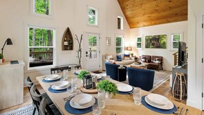 Un vaste espace dédié à la salle à manger, avec une longue table en bois pouvant accueillir six personnes, entourée de grandes fenêtres offrant une vue sur l’extérieur.