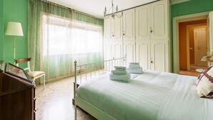 A bedroom with a bed, a chair, a dresser, a chandelier, and a wardrobe.