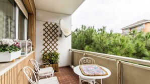 A balcony with a white table and chairs, a satellite dish, and a view of green trees.