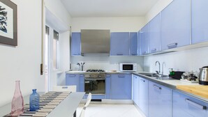 A modern kitchen with blue cabinets, a stainless steel range hood, a microwave, and a wooden countertop.