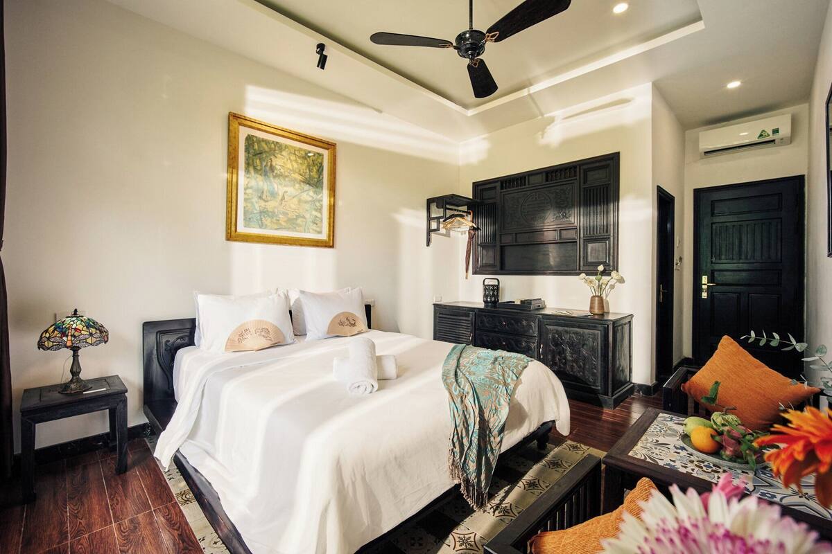 Une chambre bien éclairée, avec un lit, une table de chevet et un ventilateur de plafond.