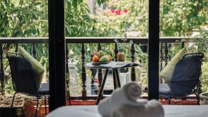 Un balcón con dos sillas, una mesa pequeña con frutas y un jarrón, y vista a exuberante vegetación.