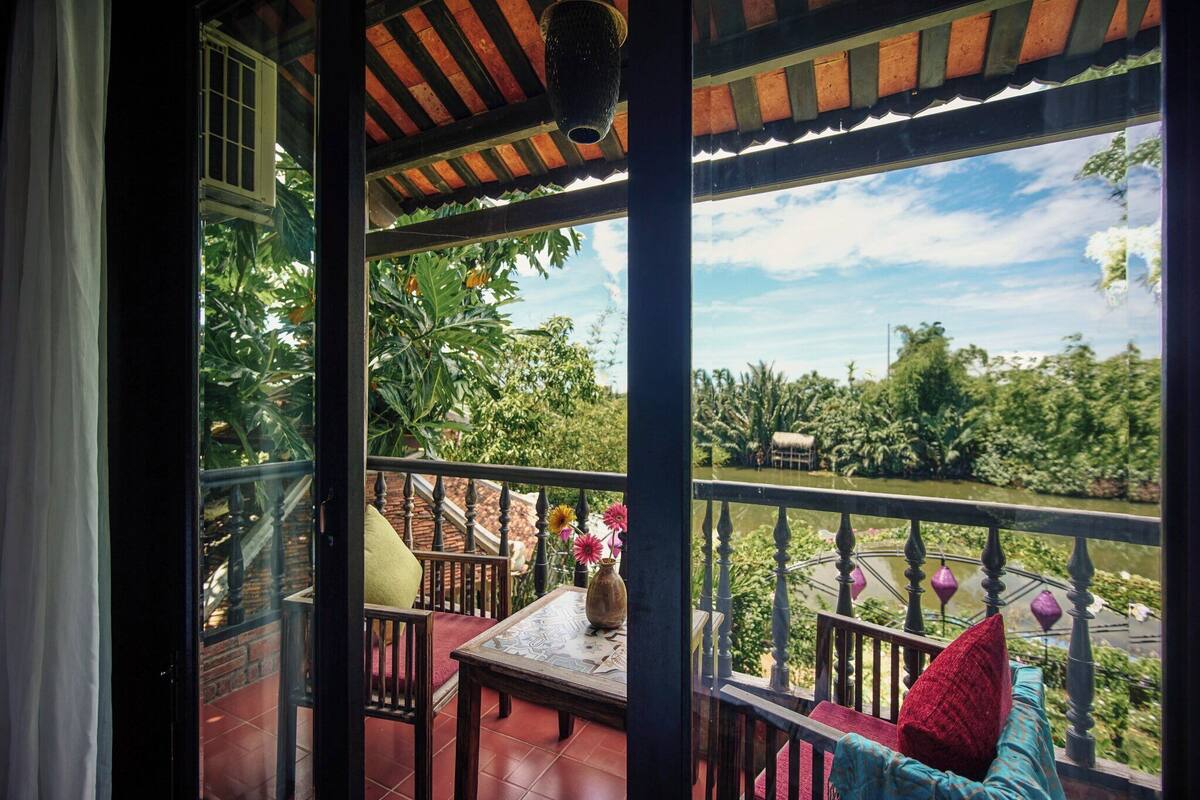 Un balcon avec une table, des chaises et une vue sur un jardin et un plan d’eau.
